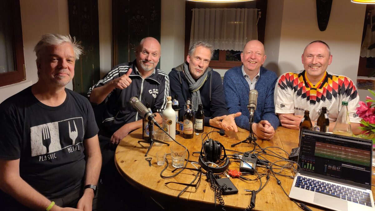 Ralf, Hubertus, Andreas, Manfred und Alex an einem Küchentisch nach der Aufnahme der Podcast-Episode. Auf dem Tisch stehen und liegen ein Notebook, viele Kabel, Mikrophone und Kopfhörer.
